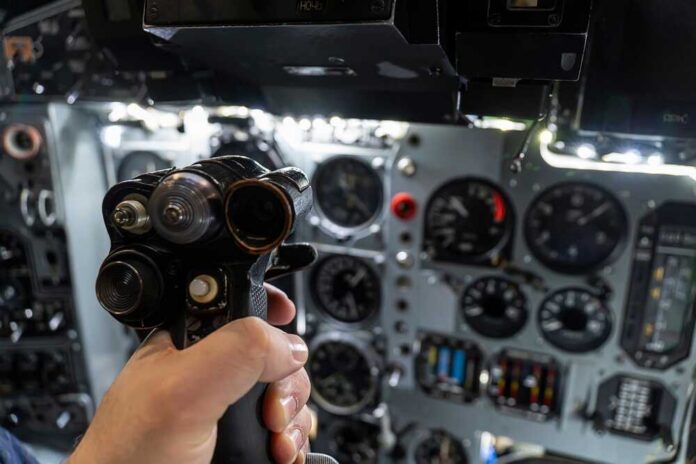 Helm,Of,A,Military,Helicopter,In,The,Pilot's,Hand.,Fighter A hand holding a cockpit control device in an aircraft cockpit
