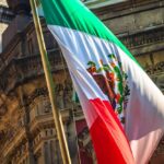 Mexico Targets ICE With Homicide Claims Mexican flag waving in front of an ornate stone building