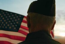 AI Denials Hit Veteran Families Hard A veteran in uniform standing in front of an American flag at sunset