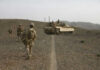 Soldiers walking with armored tank in desert landscape