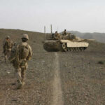 Autonomous Mine-Layer Raises Hacking Fears Soldiers walking with armored tank in desert landscape