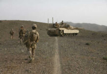Soldiers walking with armored tank in desert landscape