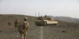 Soldiers walking with armored tank in desert landscape