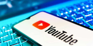 YouTube app on smartphone over illuminated laptop keyboard
