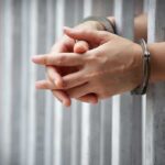 hands in handcuffs behind jail bars