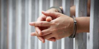 hands in handcuffs behind jail bars
