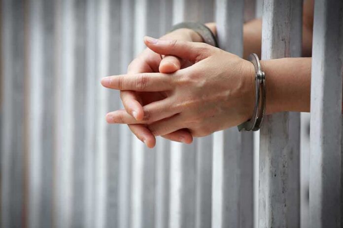 hands in handcuffs behind jail bars