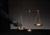 Judge FREEZES Trump TPS Kill Switch Golden balance scale with gloved hand pressing one pan