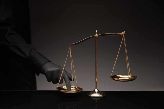 shutterstock_1069895747-1 Golden balance scale with gloved hand pressing one pan