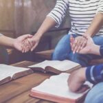 People holding hands around open books on a table
