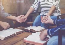People holding hands around open books on a table