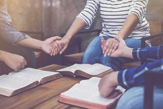 shutterstock_1069961357 People holding hands around open books on a table