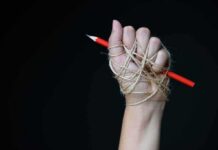 Customs Law Twist Targets Journalists Hand wrapped in twine gripping a red pencil