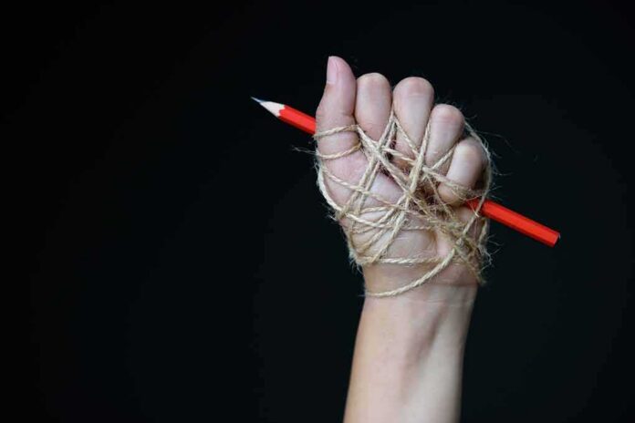 Hand wrapped in twine gripping a red pencil