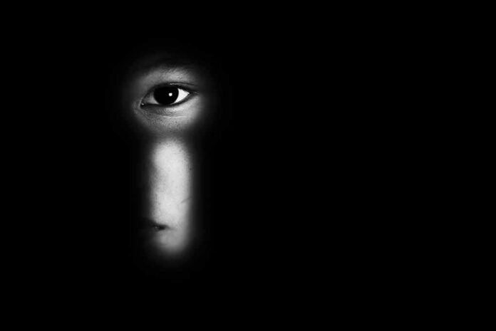 face peering through a keyhole in darkness