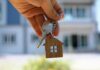 Verification Gaps Let Illegals In—For Now Hand holding house keys with a wooden house keychain