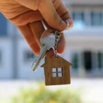 Hand holding house keys with a wooden house keychain