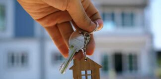 Hand holding house keys with a wooden house keychain