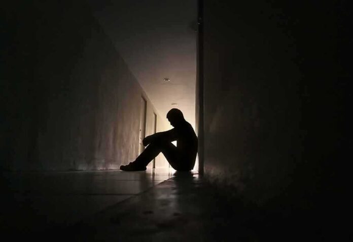 shutterstock_1502365082 Silhouette of a person sitting on the floor in a dim hallway
