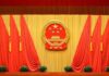 Beijing’s ‘Science’ Base Turns Menacing Chinese national emblem on red-draped stage backdrop