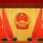 Beijing’s ‘Science’ Base Turns Menacing Chinese national emblem on red-draped stage backdrop
