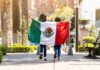two people walking with a Mexican flag on a sunny city street