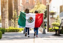 two people walking with a Mexican flag on a sunny city street
