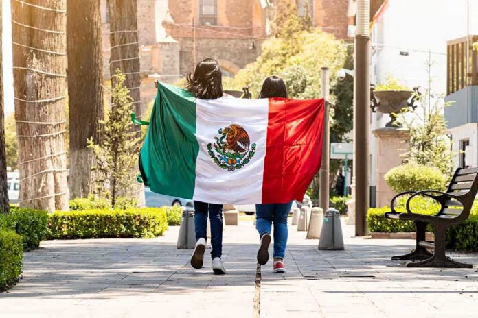 shutterstock_2021235449 two people walking with a Mexican flag on a sunny city street