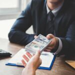 Businessperson hands over a stack of US dollars across a desk