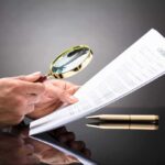 State AG Pounces: Big Tech Immunity Fantasy COLLAPSES Hands holding magnifying glass over contract document