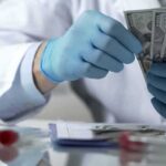 Pritzker’s Slimdown – Costly Meds Hit Taxpayers Gloved hands in a lab coat counting US dollar bills