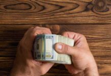 Hands holding a thick stack of U.S. hundred-dollar bills