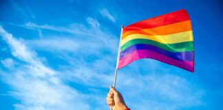 Hand holding a rainbow pride flag against a blue sky