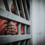 COVID Gamble: Early Release Backfires – Murder Charges Follow Hand gripping jail bars
