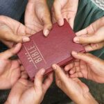 Multiple hands holding a red Bible