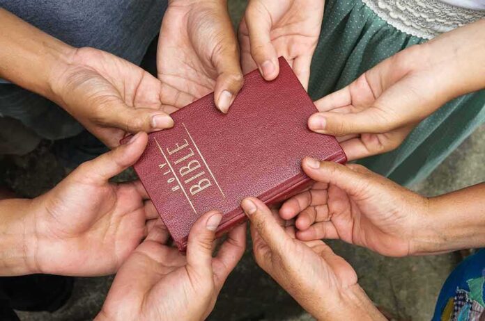 shutterstock_133452947 Multiple hands holding a red Bible