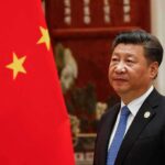 Seven Sites – China’s Nuke Buildout Accelerates Xi Jinping standing beside a Chinese flag