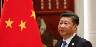 Xi Jinping standing beside a Chinese flag