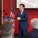 Senator Nukes Congressman—Family Bombshell Erupts Speaker in a navy suit addressing an audience at a podium
