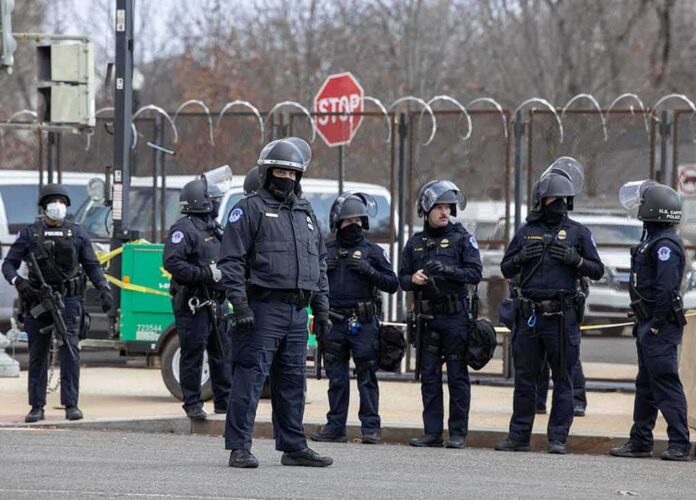 Group of police officers in riot gear standing on a street; Brian Folkerts present