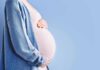 Pregnant person holding belly in blue cardigan