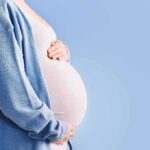 Pregnant person holding belly in blue cardigan