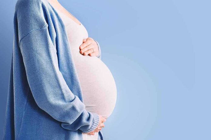 Pregnant person holding belly in blue cardigan
