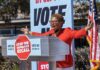 Money Vanished? HUD Freezes LA Homeless Funds Speaker at outdoor rally behind podium with vote signs