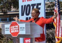 Money Vanished? HUD Freezes LA Homeless Funds Speaker at outdoor rally behind podium with vote signs