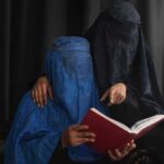 Two veiled women reading a red book together