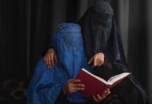 Two veiled women reading a red book together