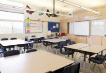 Teacher Axed Over Side Hustle? Policy Mystery Deepens Empty classroom with tables, chairs, and a whiteboard