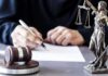 Money Trail Topples $20M Migrant Pipeline Judge writing at desk with gavel and Lady Justice statue