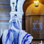 Synagogue Shock: Teen Slashed Mid-Prayer Person in white and blue prayer shawl facing ornate interior